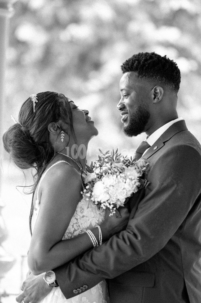 Un couple en tenue de mariage s'enlace et se regarde avec tendresse dans un cadre extérieur flou.