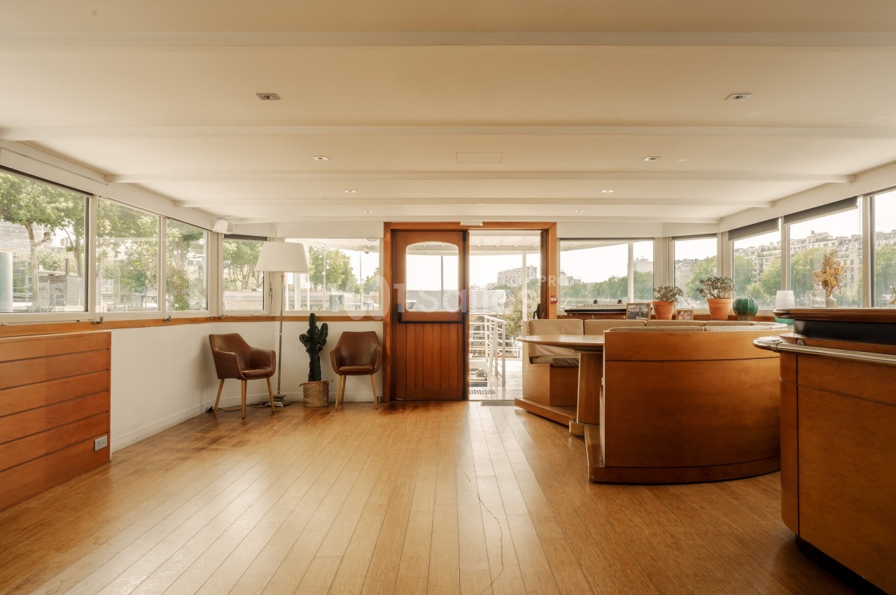 Intérieur lumineux avec parquet, mobilier en bois, grandes fenêtres et vue sur un espace extérieur.