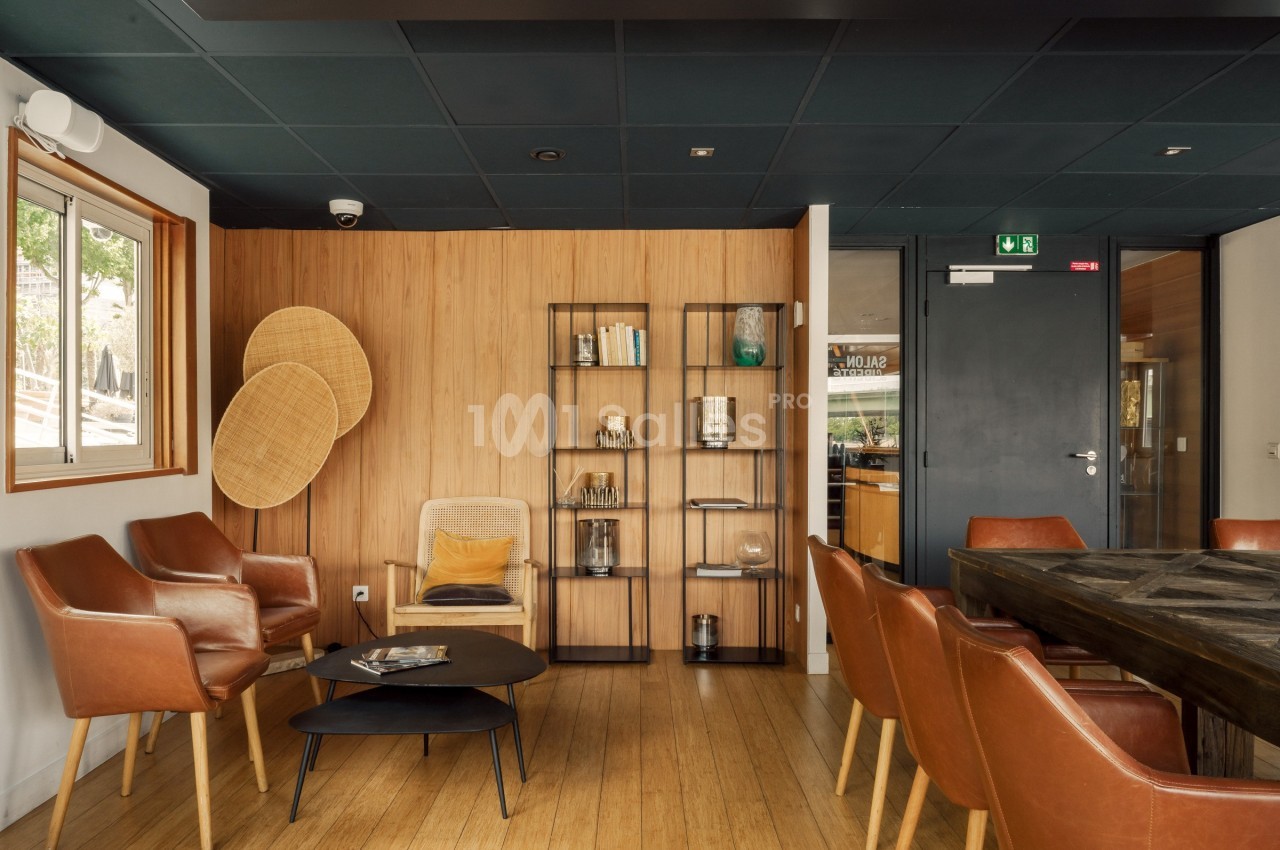 Salle de réunion chaleureuse avec des fauteuils en cuir, une table en bois, étagères décoratives et un mur en bois clair.