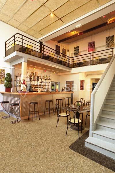 Intérieur d'un café moderne avec un bar, des tables, des chaises et une mezzanine accessible par un escalier.