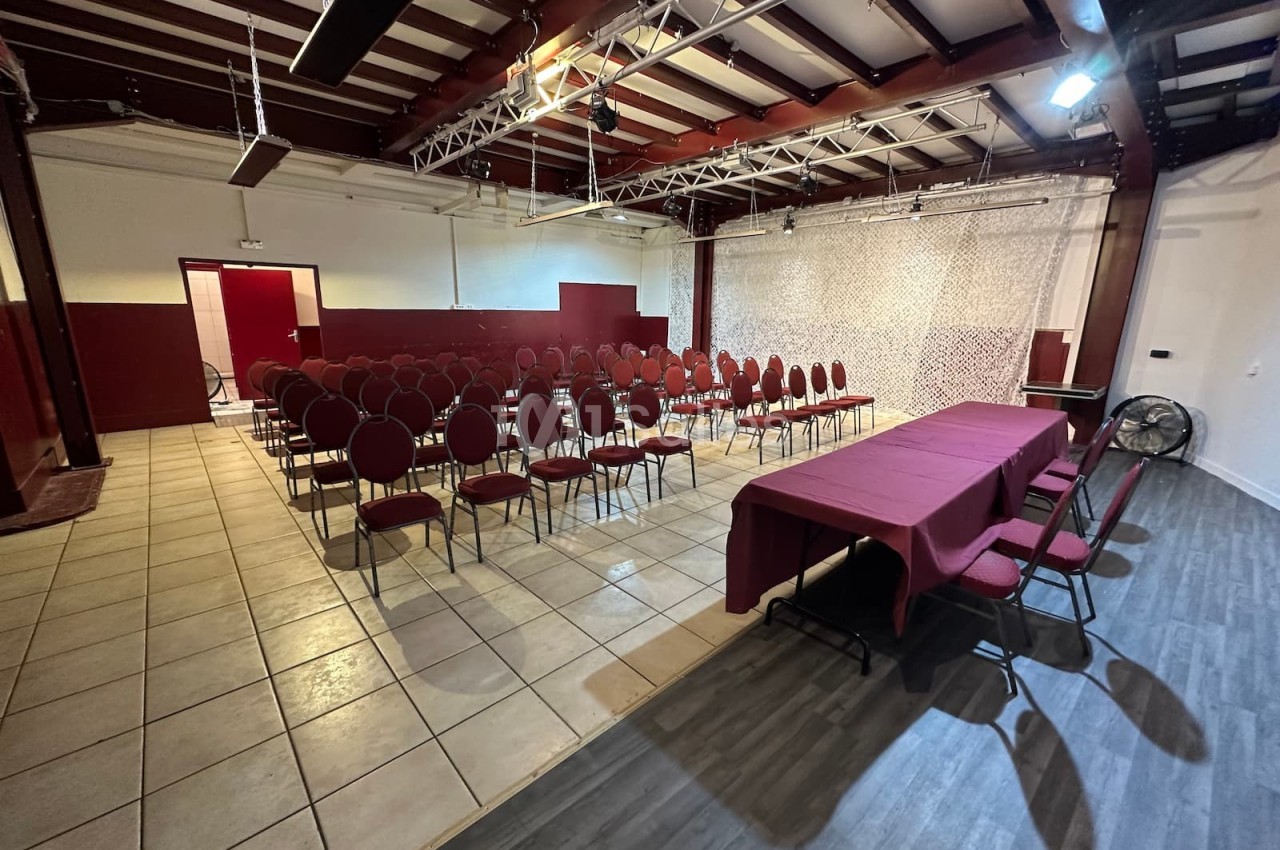 Salle de conférence avec rangées de chaises rouges alignées face à une table recouverte d'une nappe bordeaux.