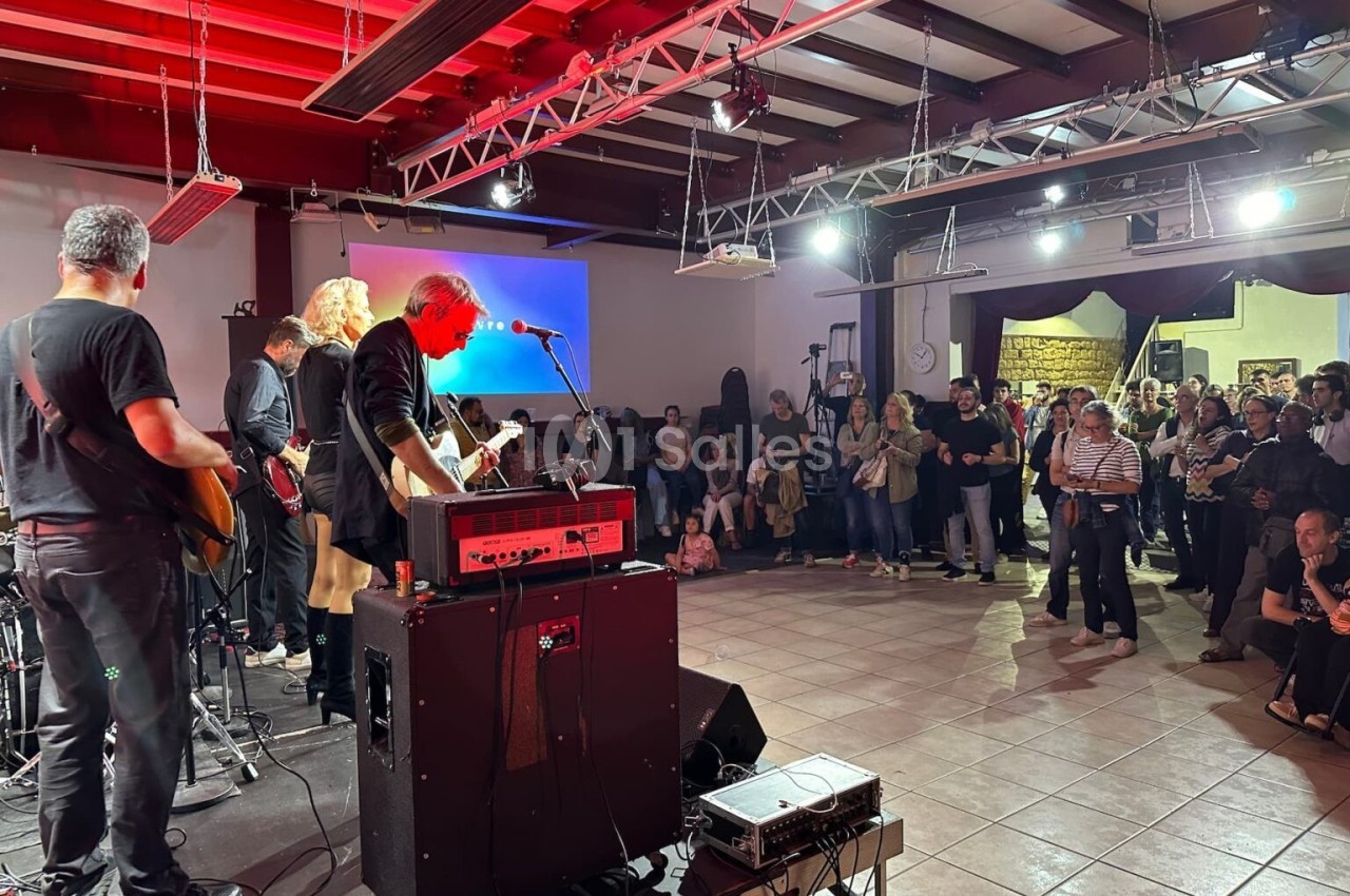 Un groupe de musiciens joue sur scène dans une salle, devant un public debout et attentif.