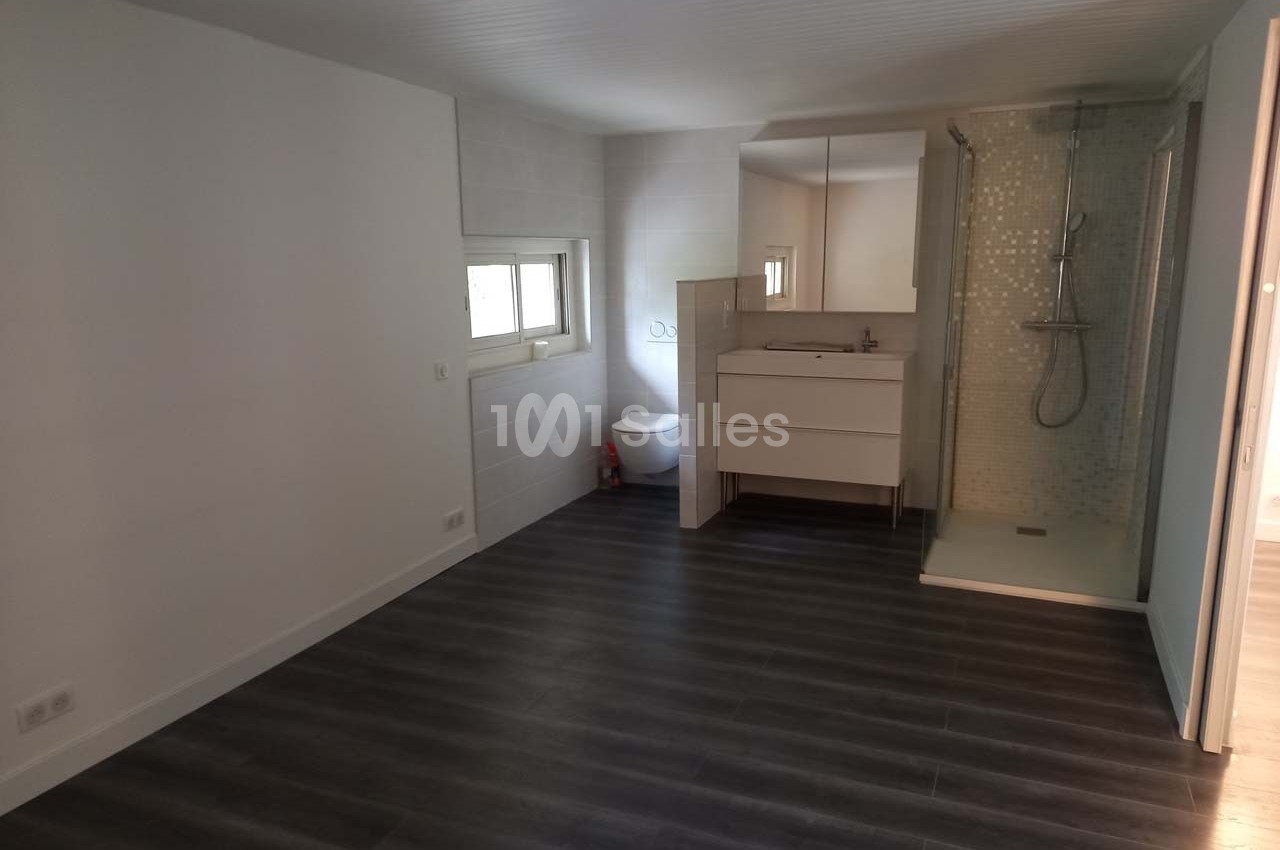 Chambre avec sol en parquet sombre, salle d'eau intégrée comprenant douche, lavabo et toilettes, éclairée par une fenêtre.