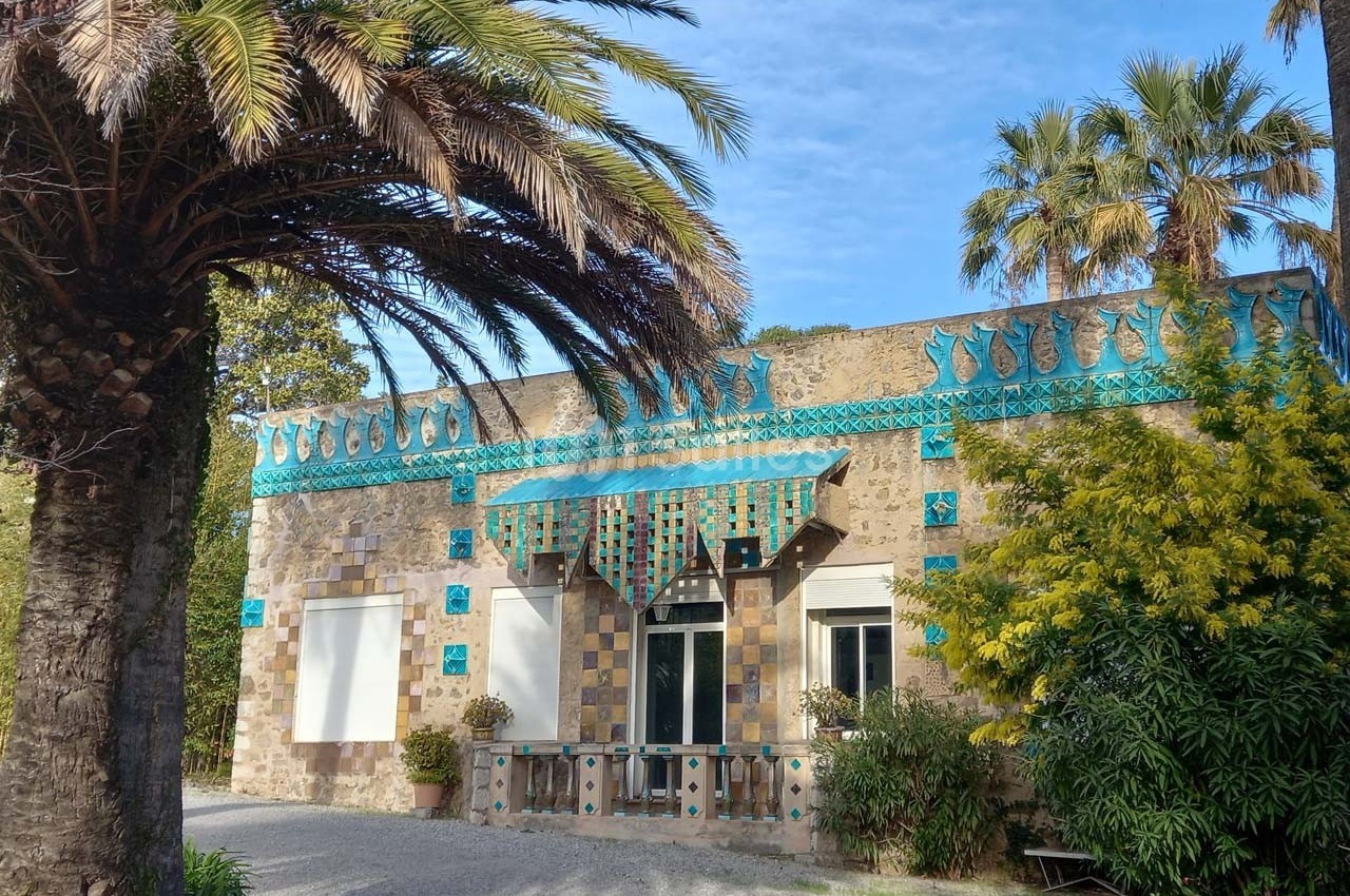 Façade d'un bâtiment en pierre décoré de mosaïques bleues et vertes, entouré de palmiers et de végétation.