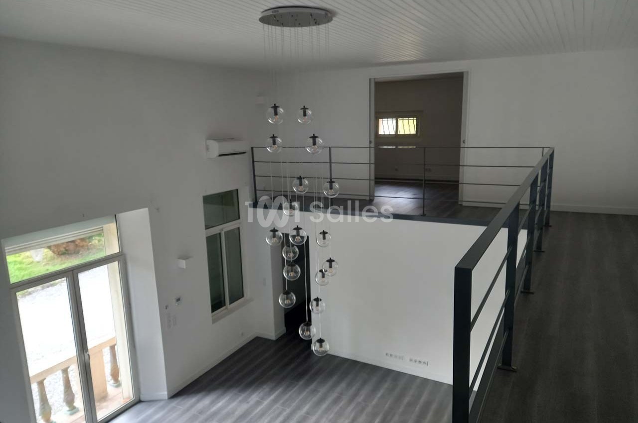 Intérieur d'une pièce lumineuse avec mezzanine, sol en parquet gris, grandes fenêtres et suspension moderne.