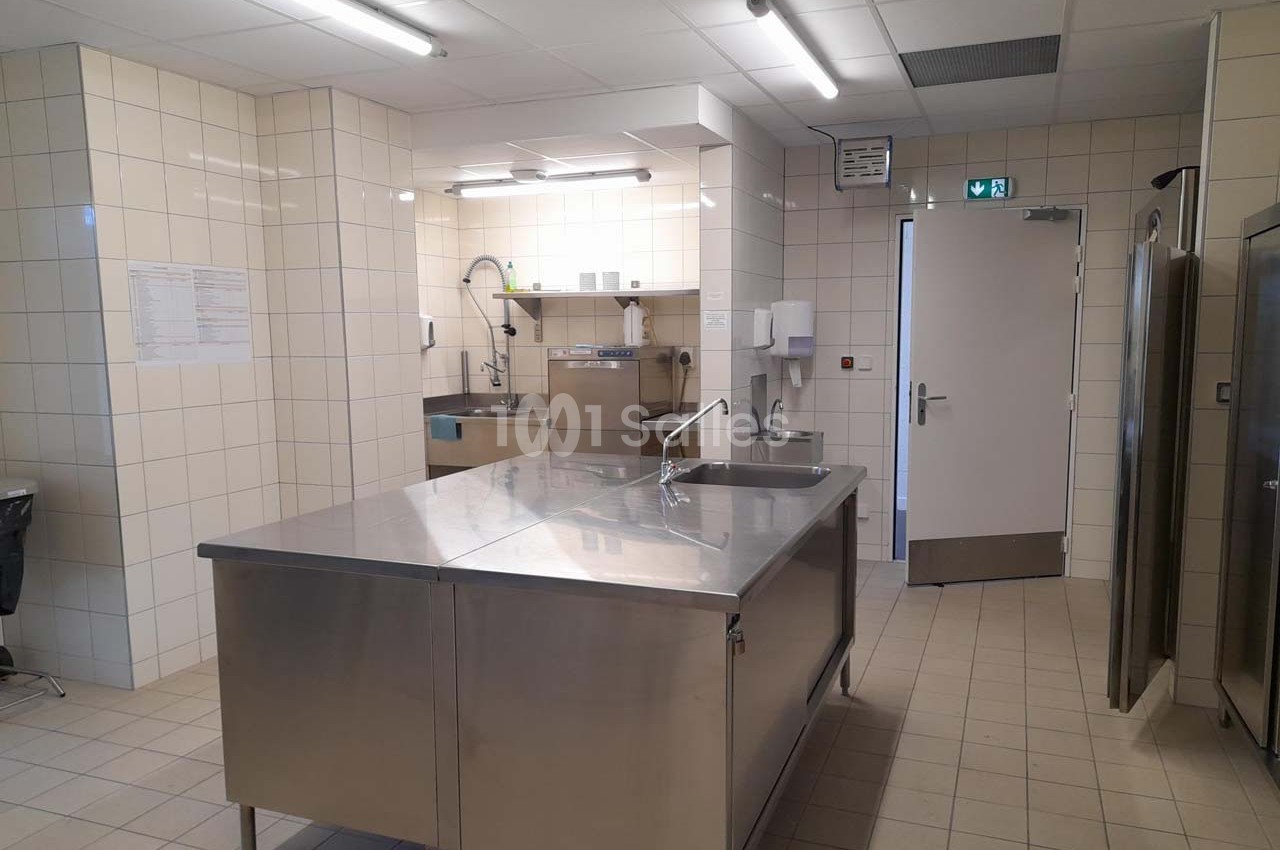 Cuisine professionnelle avec plan de travail en inox, équipements de lavage, carrelage mural et sol clair.