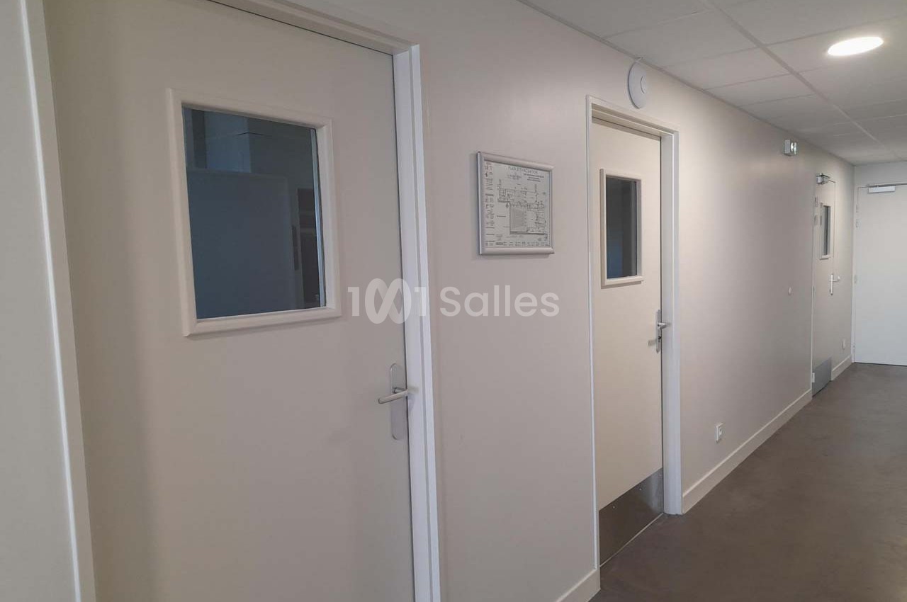 Couloir intérieur avec portes blanches équipées de fenêtres rectangulaires et un éclairage au plafond.