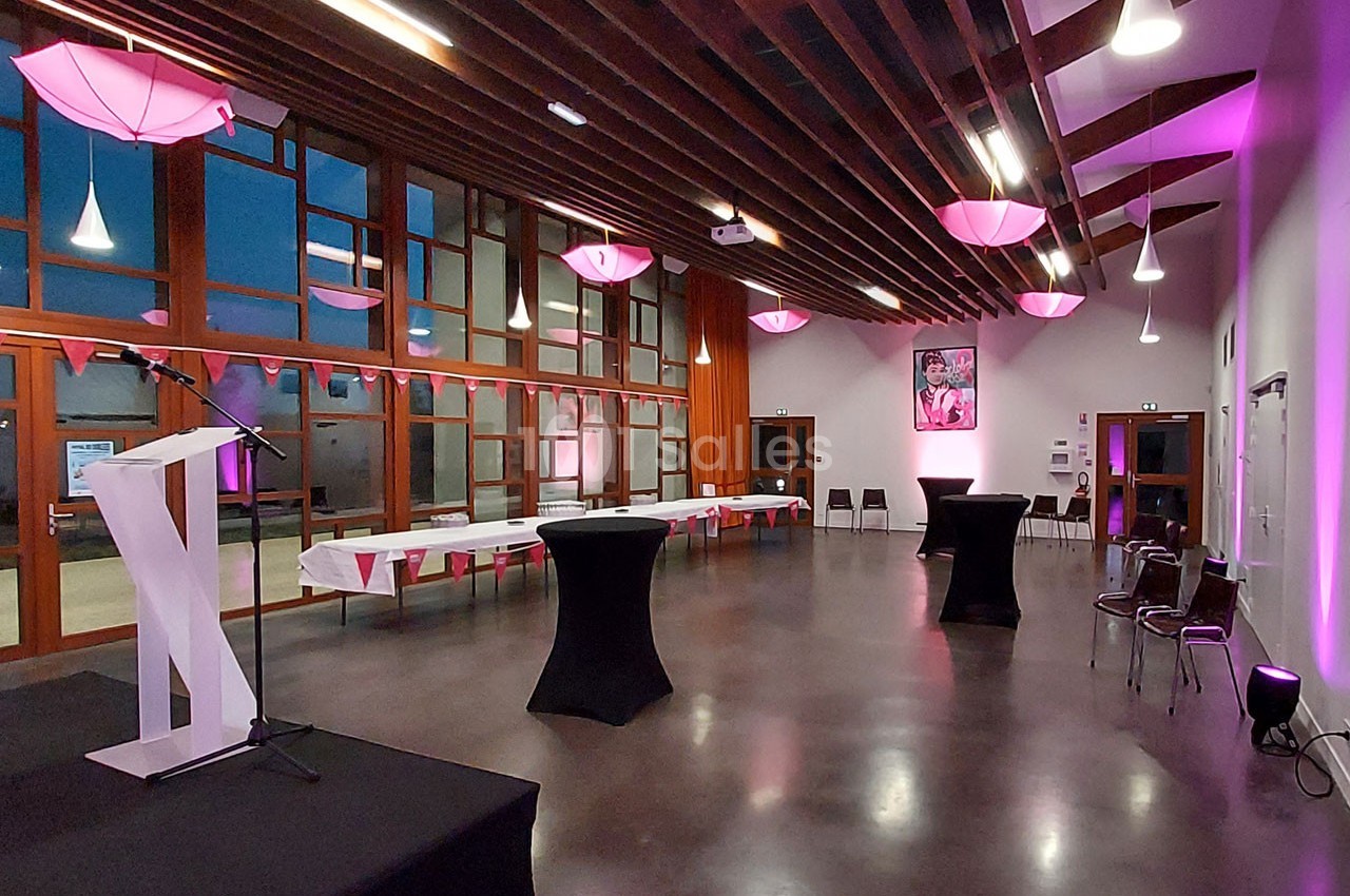 Salle de réception moderne avec tables dressées, chaises alignées et éclairage rose diffus sous un plafond en bois.