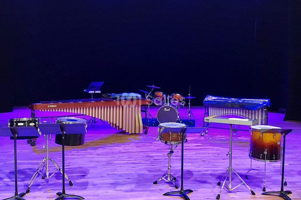 Ensemble d'instruments de percussion sur une scène éclairée, comprenant marimba, batterie et divers tambours.