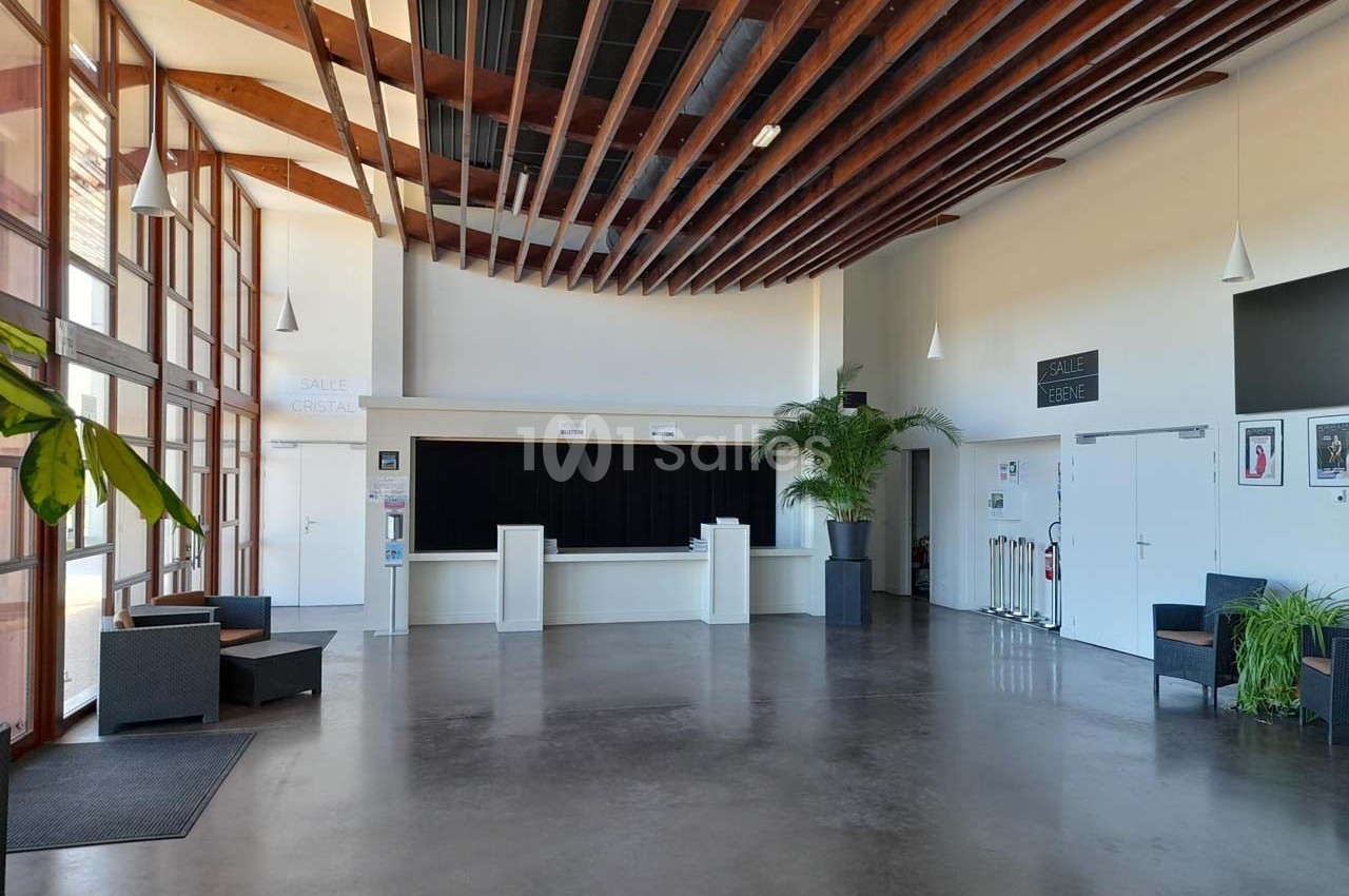 Hall lumineux avec sol en béton, plafond en bois, comptoir d'accueil, plantes et mobilier moderne.