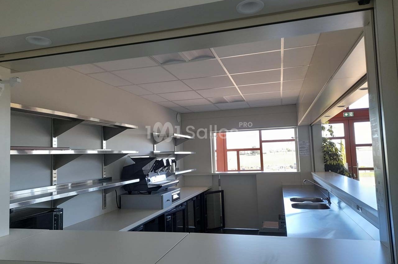 Cuisine professionnelle moderne avec plans de travail en inox, étagères murales et grandes fenêtres laissant entrer la…