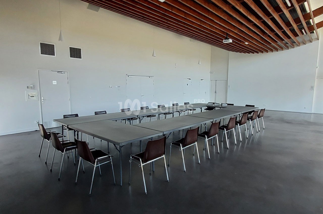 Salle de réunion vide avec une grande table en U entourée de chaises, plafond en bois et sol en béton poli.