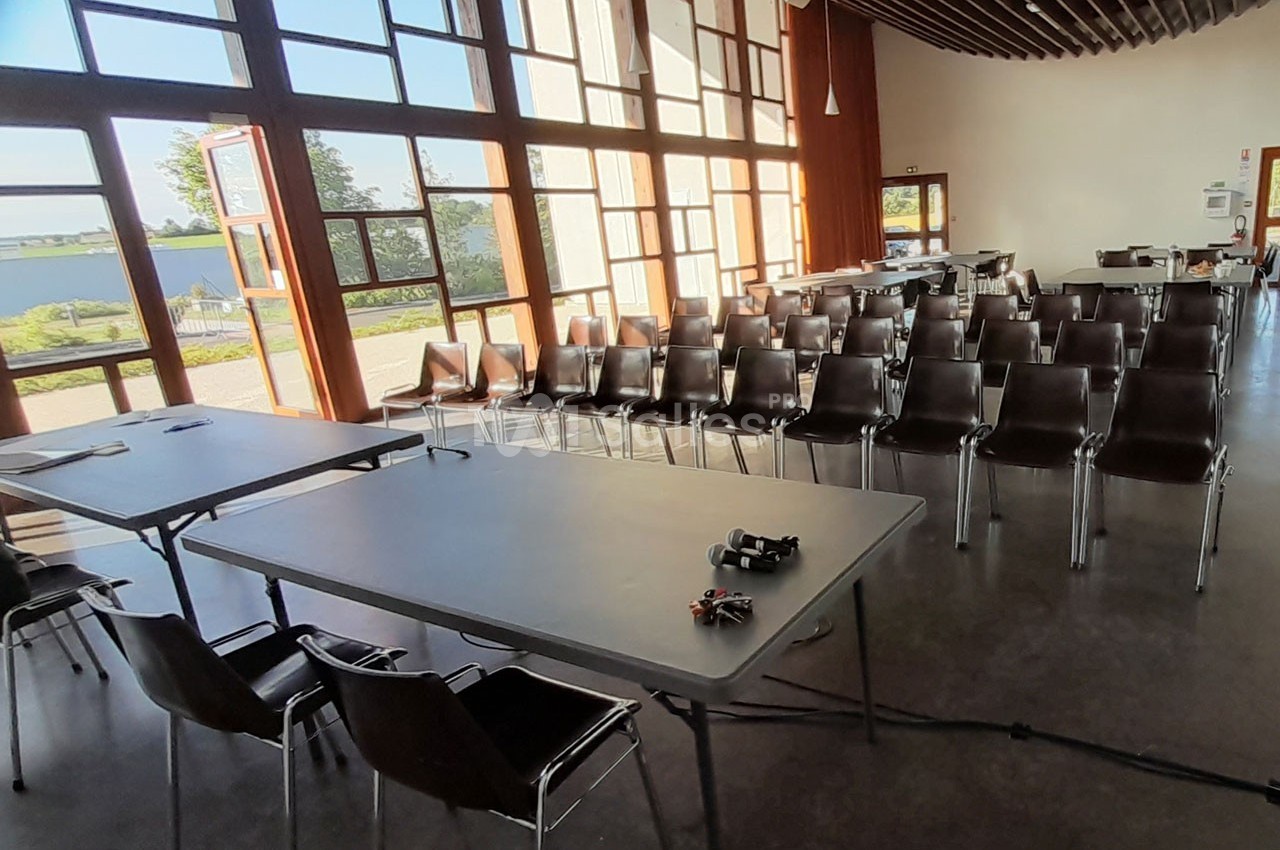 Salle de réunion lumineuse avec des rangées de chaises alignées et deux tables équipées d'accessoires.