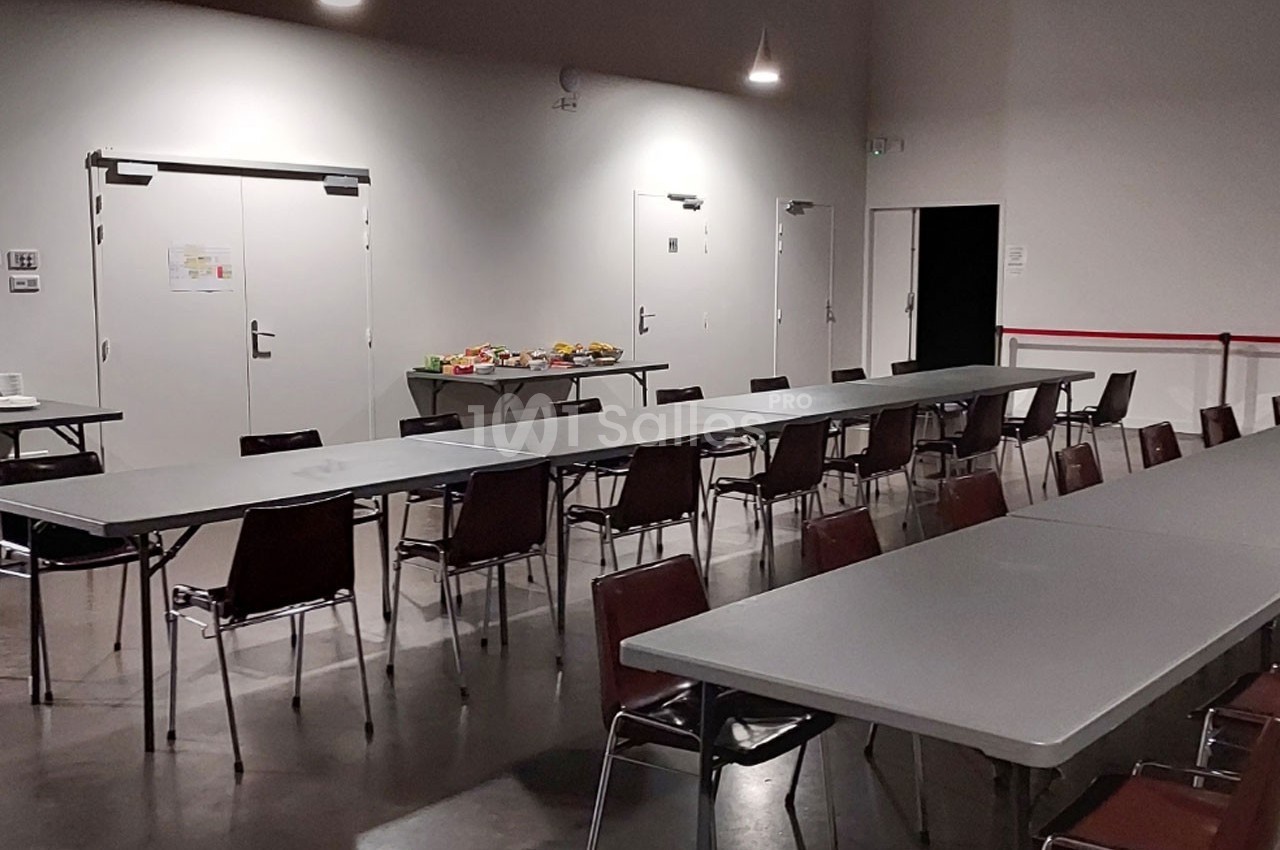 Salle avec des tables et chaises alignées, un buffet disposé au fond près des portes blanches.