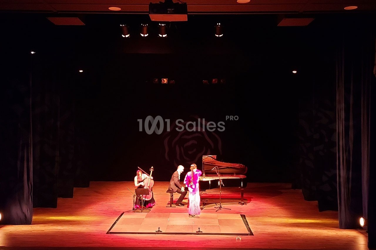 Deux musiciens jouant du piano et du violoncelle accompagnent une chanteuse sur une scène éclairée.