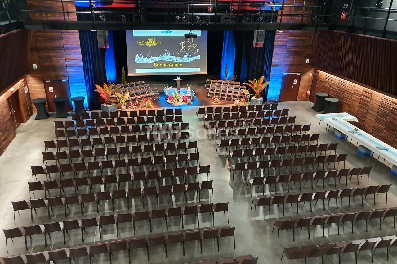 Salle de conférence aménagée avec des rangées de chaises, une scène décorée et un écran affichant ’Bonne Année’.