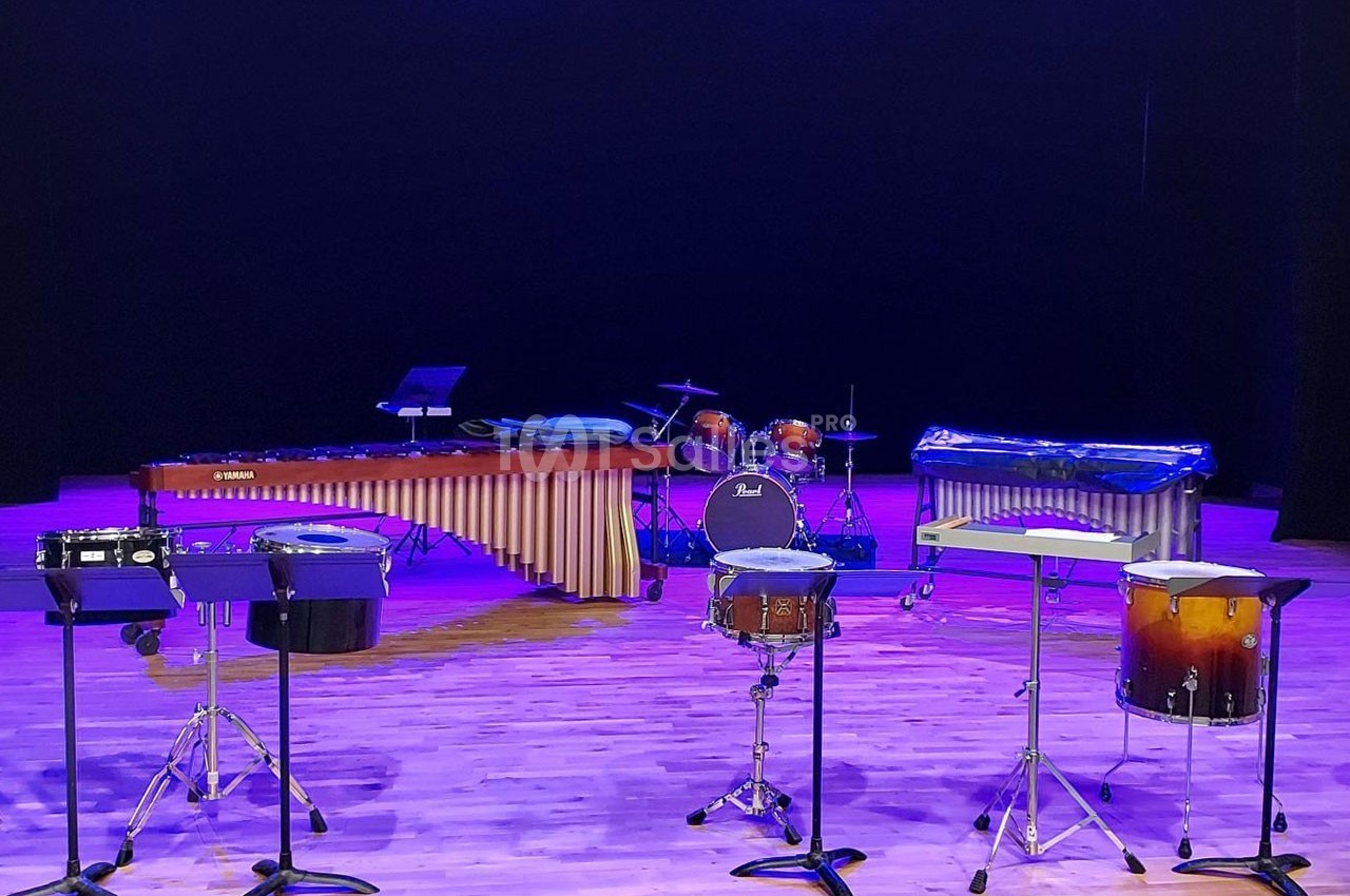 Ensemble d'instruments de percussion, incluant marimba, batterie et tambours, disposés sur une scène éclairée.