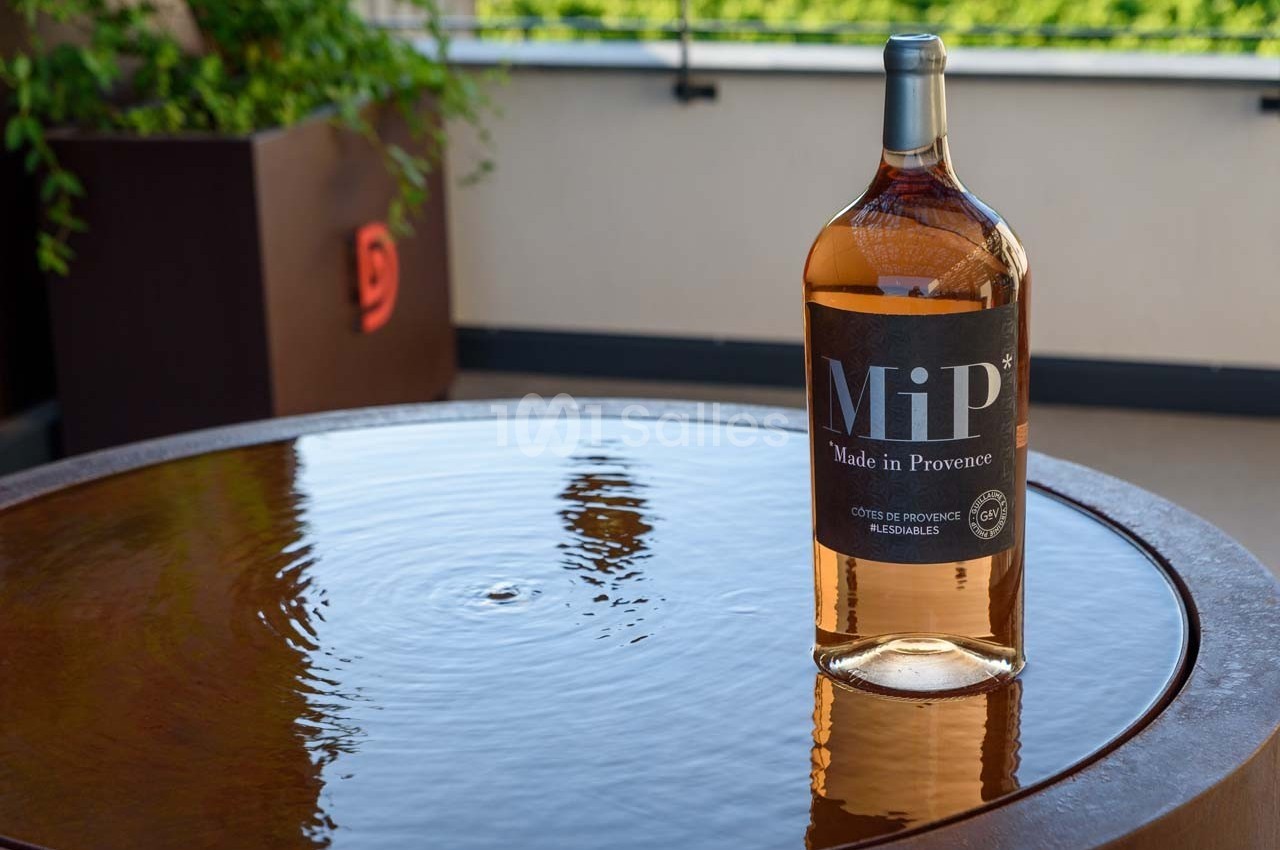 Bouteille de vin rosé posée sur une table ronde en métal avec des reflets d'eau, en extérieur.