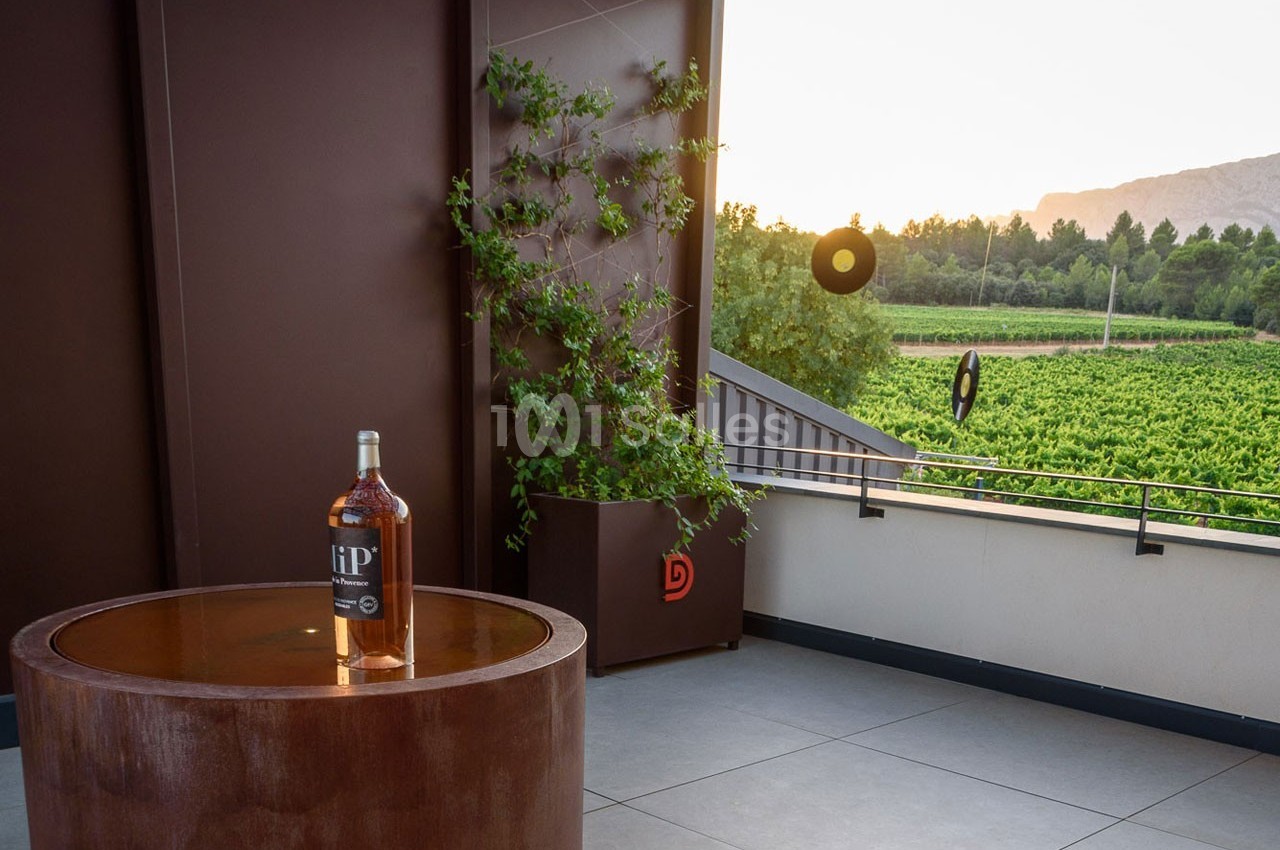 Bouteille de spiritueux posée sur une table ronde en terrasse avec vue sur un vignoble au coucher du soleil.