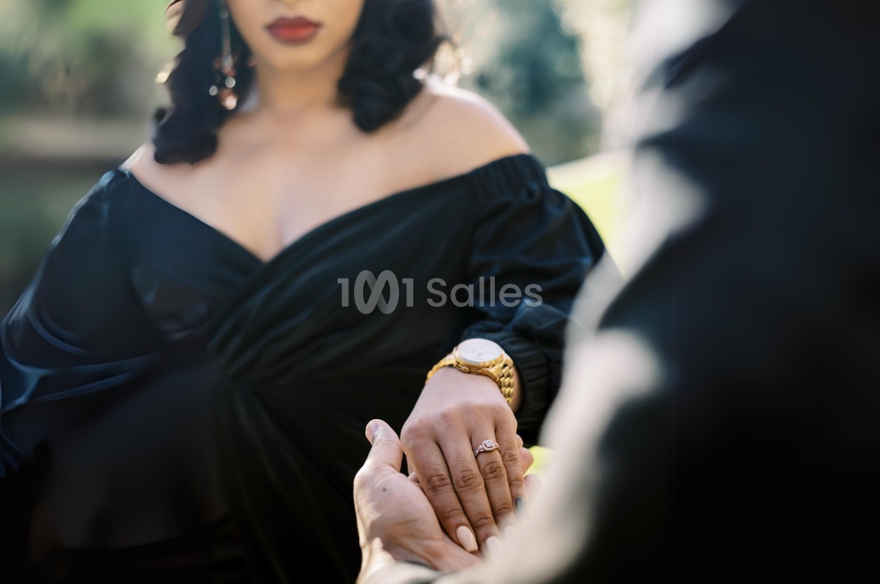 Une femme en robe noire tient la main d'une autre personne dans un cadre extérieur lumineux.