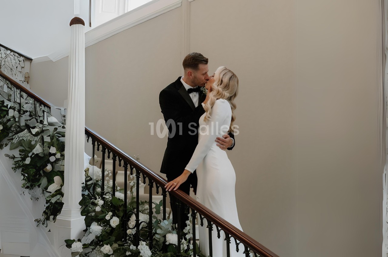 Un couple élégant s'embrasse sur un escalier décoré de fleurs blanches et de verdure.