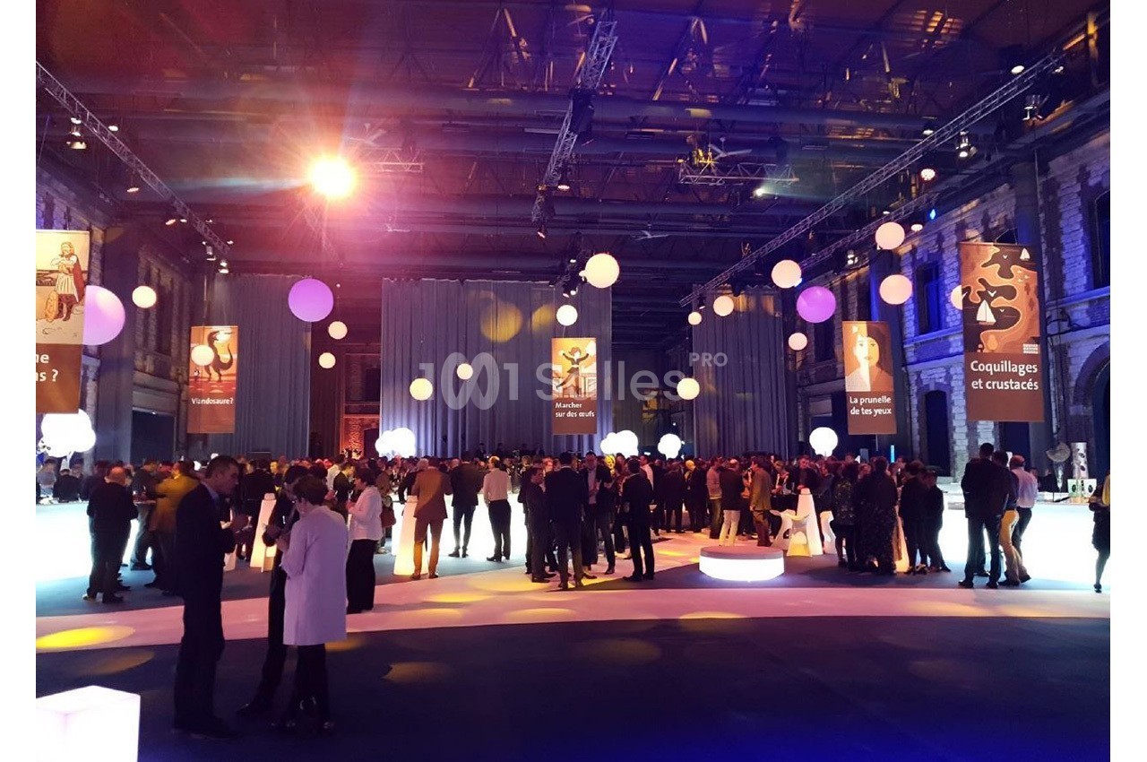 Salle événementielle avec des invités debout, éclairage coloré et décorations suspendues, ambiance festive.