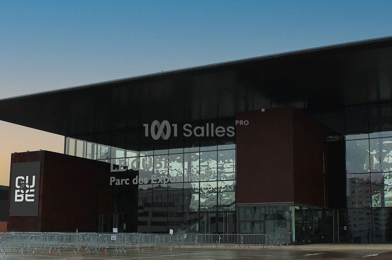 Façade moderne du bâtiment ’Le Cube’ au Parc des Expositions, avec des barrières installées à l'entrée.
