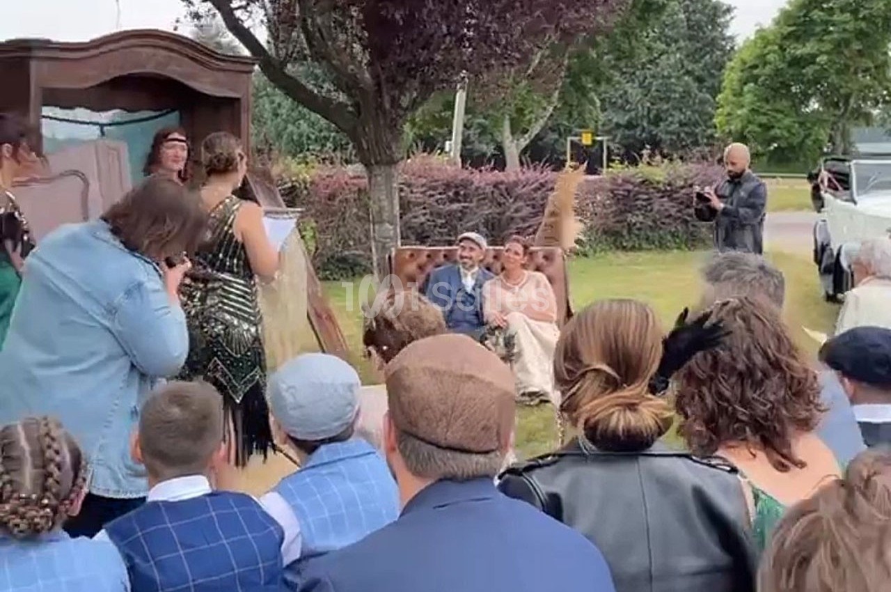 Un couple assis lors d'une cérémonie en plein air, entouré d'invités et d'un décor champêtre.