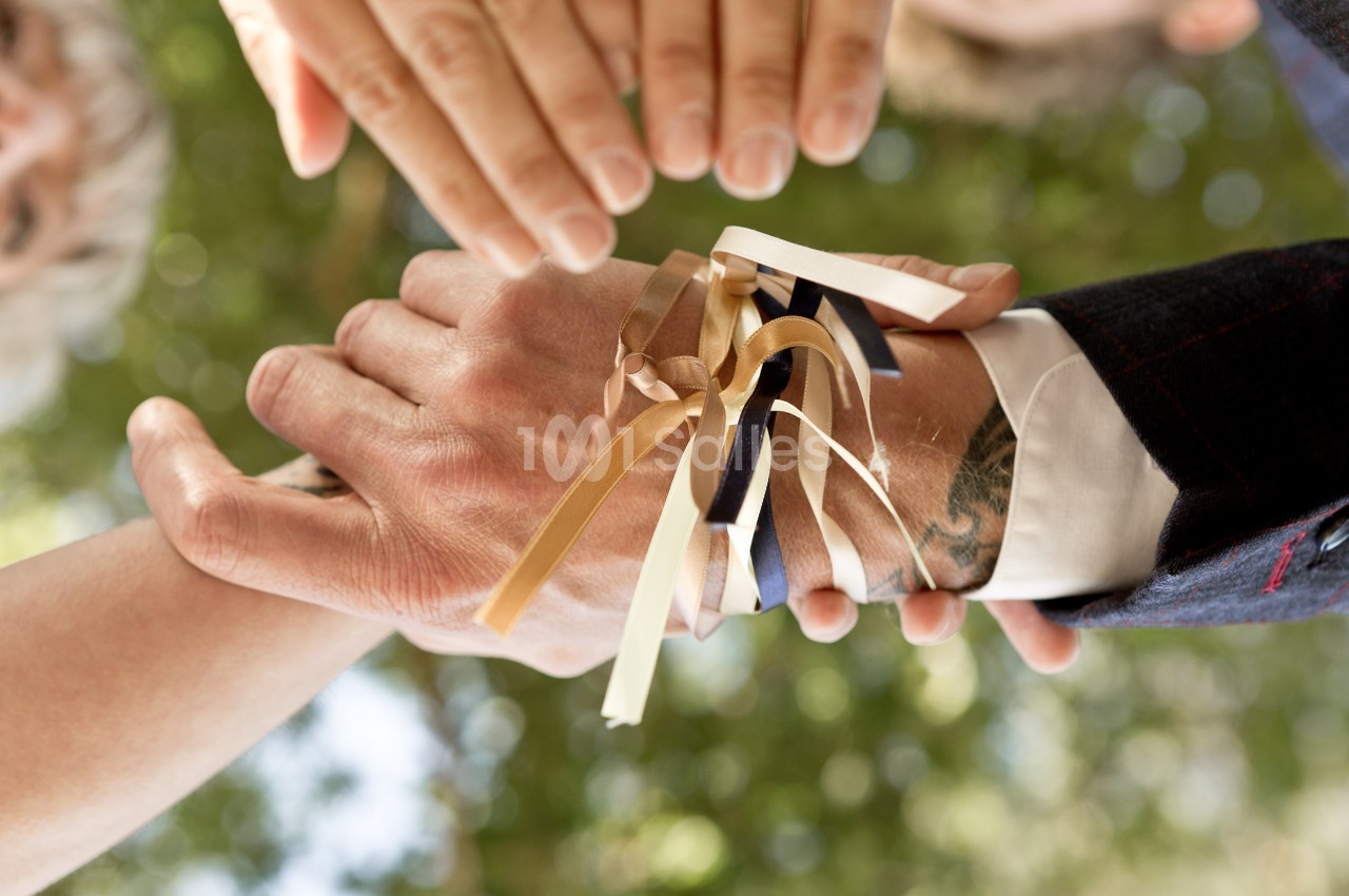 Rubans colorés noués autour des mains de deux personnes, symbolisant une union ou un rituel.
