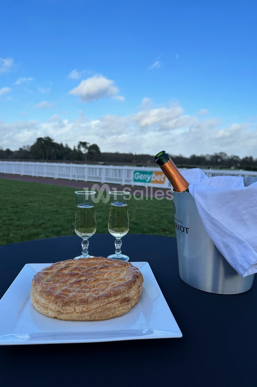 Une galette sur une assiette, deux verres de champagne et un seau avec une bouteille, en extérieur près d'un champ.