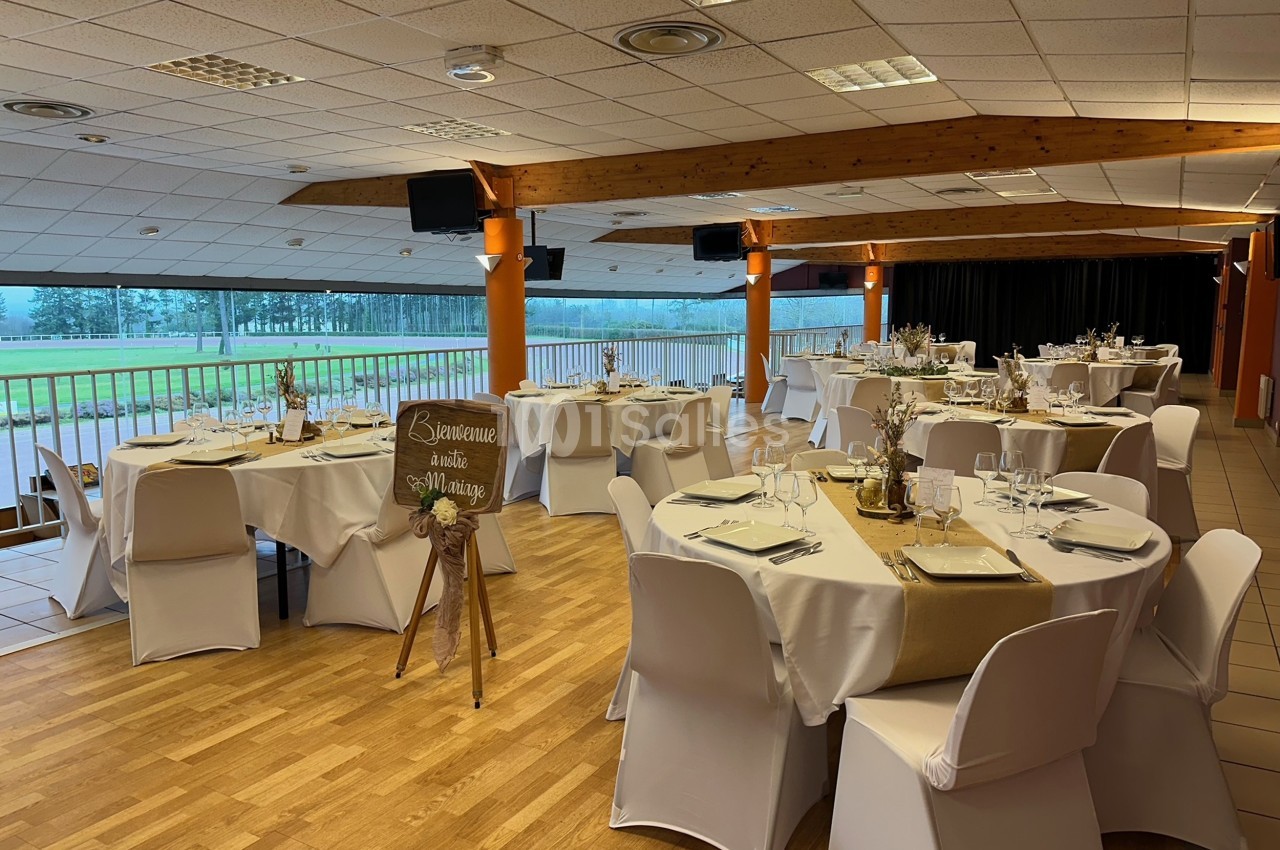 Salle de réception décorée pour un mariage, avec des tables rondes dressées et une vue sur l'extérieur.