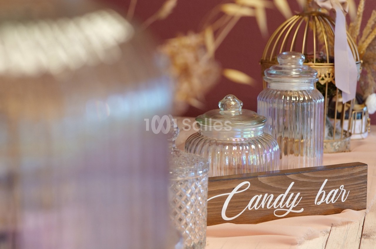 Bocaux en verre remplis de friandises sur une table avec une pancarte ’Candy bar’ en bois.