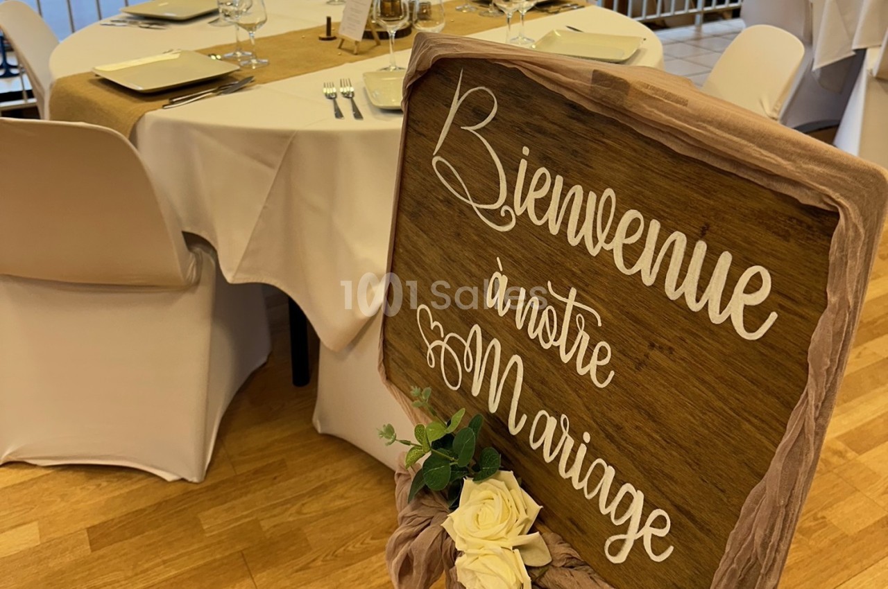 Panneau en bois avec l'inscription ’Bienvenue à notre mariage’, décoré de roses blanches, devant une table dressée.