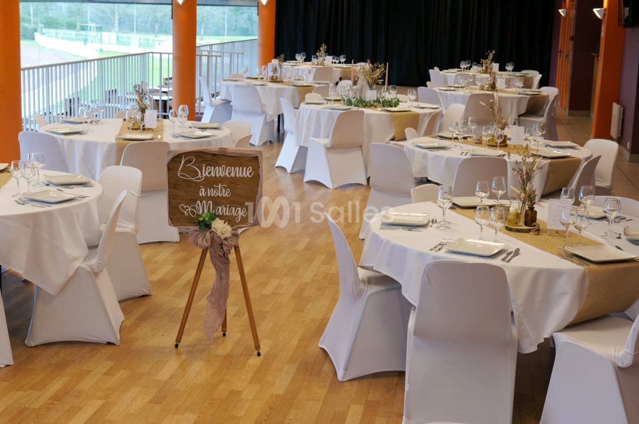 Salle de réception décorée pour un mariage, avec tables dressées et un panneau ’Bienvenue à notre mariage’.