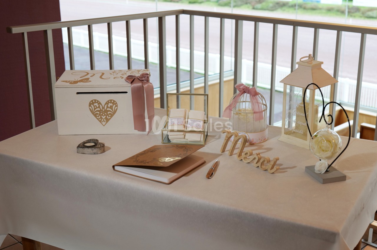 Table décorée pour un mariage avec urne, livre d'or, bougie, rubans roses et éléments en bois doré.