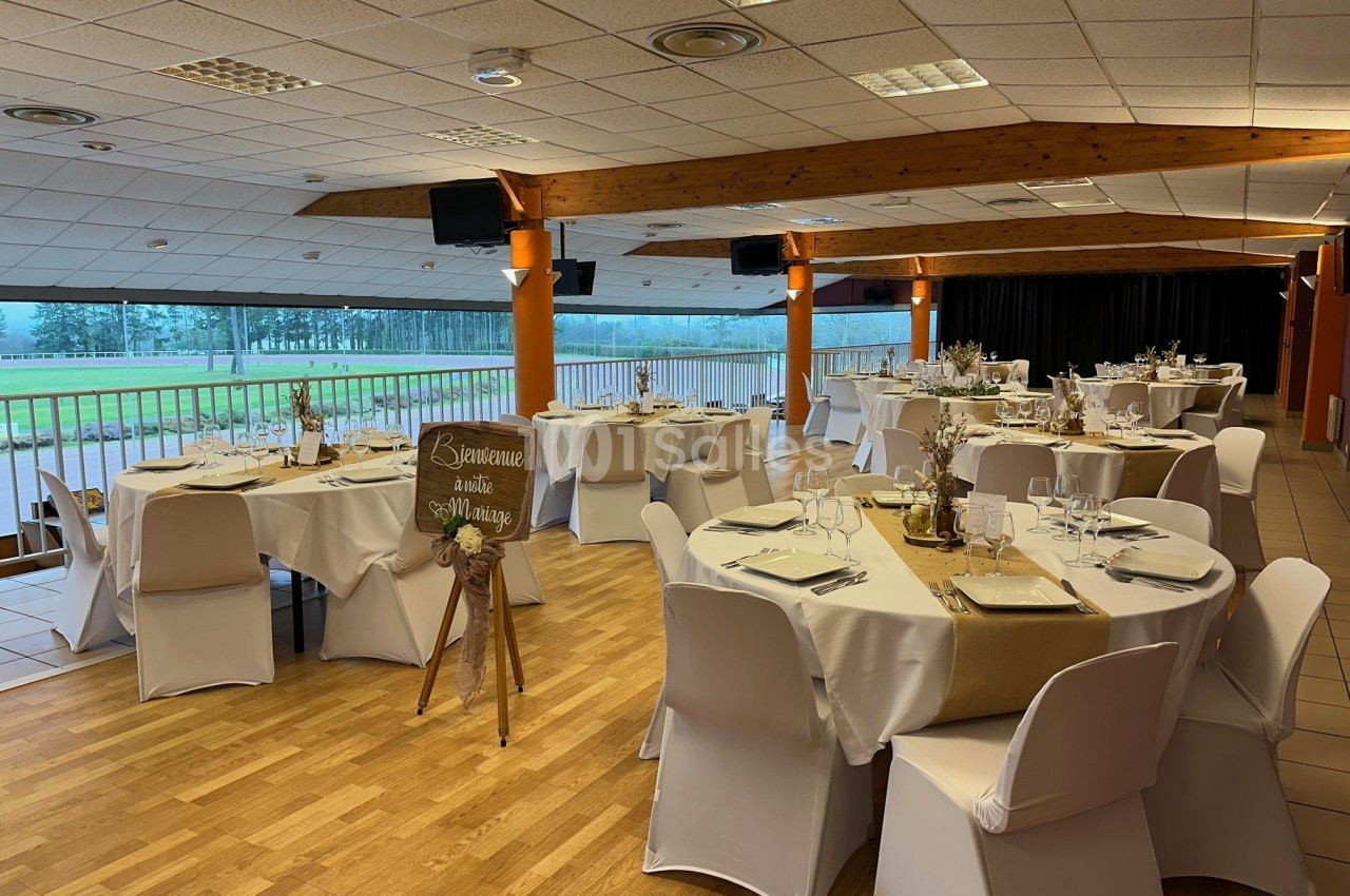 Salle de réception décorée avec des tables rondes dressées, nappes blanches et vue sur un espace extérieur verdoyant.
