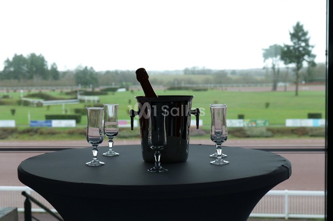 Seau à champagne avec bouteille et quatre flûtes vides sur une table, vue sur un paysage extérieur avec pelouse.