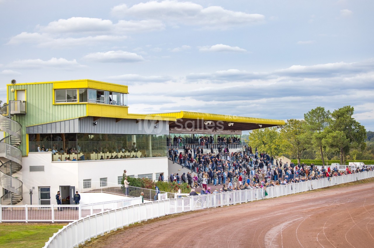Tribune d'un hippodrome avec des spectateurs rassemblés près de la piste sous un ciel légèrement nuageux.