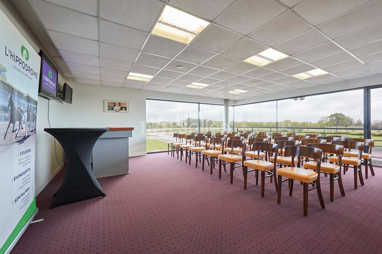 Salle de conférence lumineuse avec chaises alignées, pupitre, écran et vue sur un espace extérieur verdoyant.