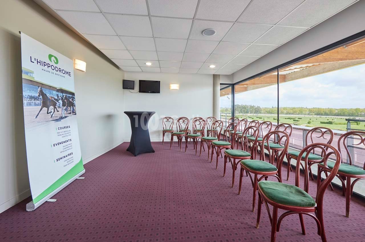 Salle de réunion avec chaises alignées, table haute et vue sur l'extérieur, affichant un panneau promotionnel de l…