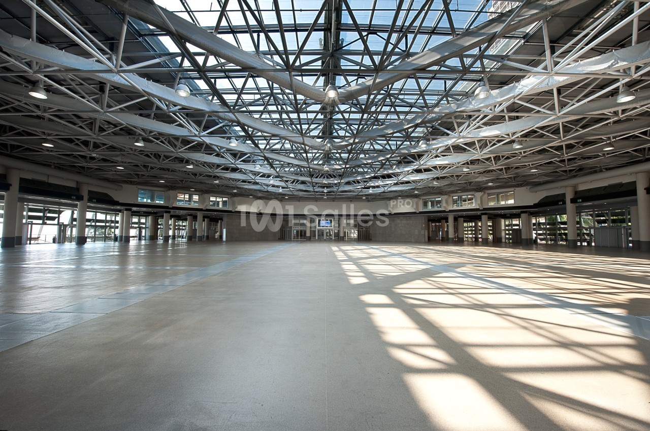 Vue intérieure d'un grand hall vide avec une structure métallique apparente et un plafond en verre laissant entrer la…