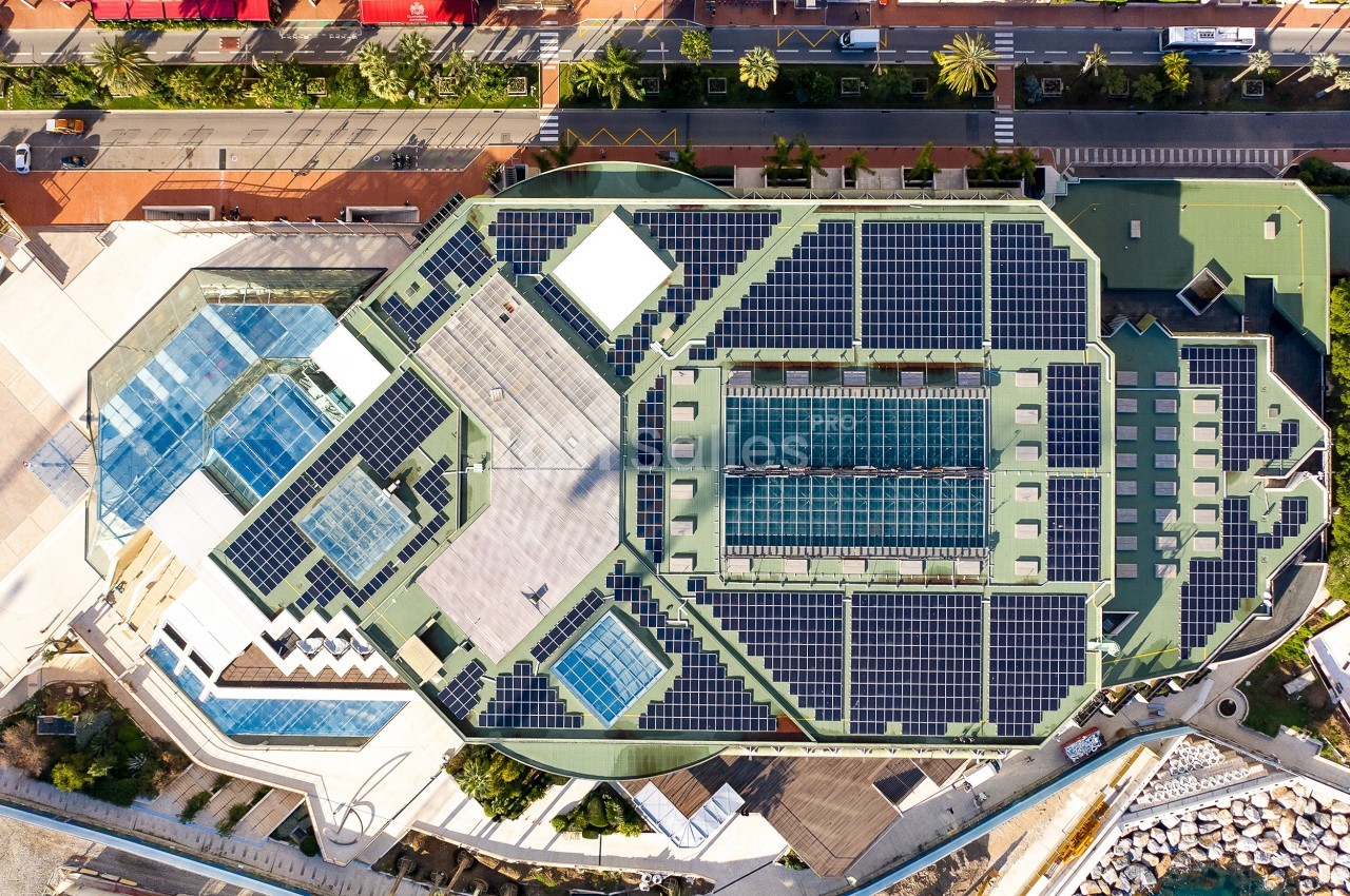 Vue aérienne d'un bâtiment avec des panneaux solaires sur le toit, entouré de routes et d'espaces urbains.