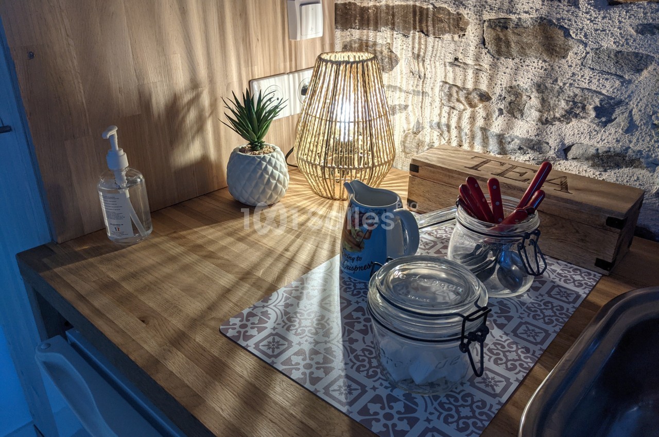 Plan de travail en bois avec lampe allumée, pot de plante, distributeur de savon, bocaux et ustensiles de cuisine.