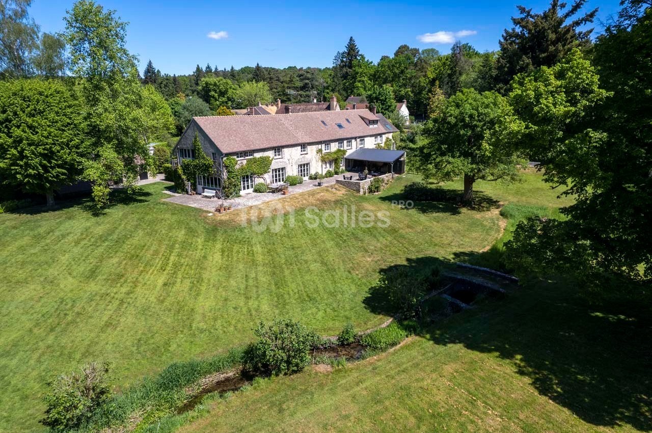 Vue aérienne d'une grande maison en pierre entourée d'un vaste jardin verdoyant avec arbres et pelouse.