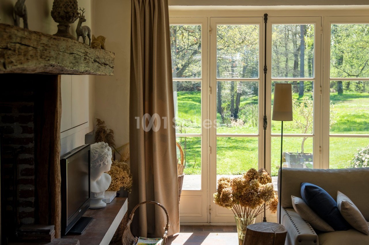 Salon lumineux avec une grande baie vitrée donnant sur un jardin verdoyant, décoré de fleurs séchées et d'éléments naturels.