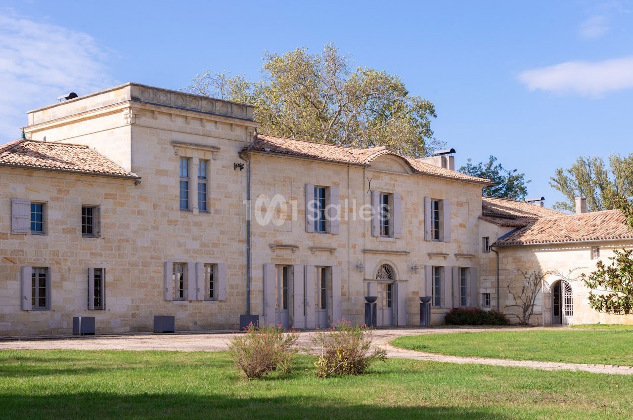 Bâtiment en pierre de style traditionnel entouré de pelouse et d'arbres sous un ciel dégagé.