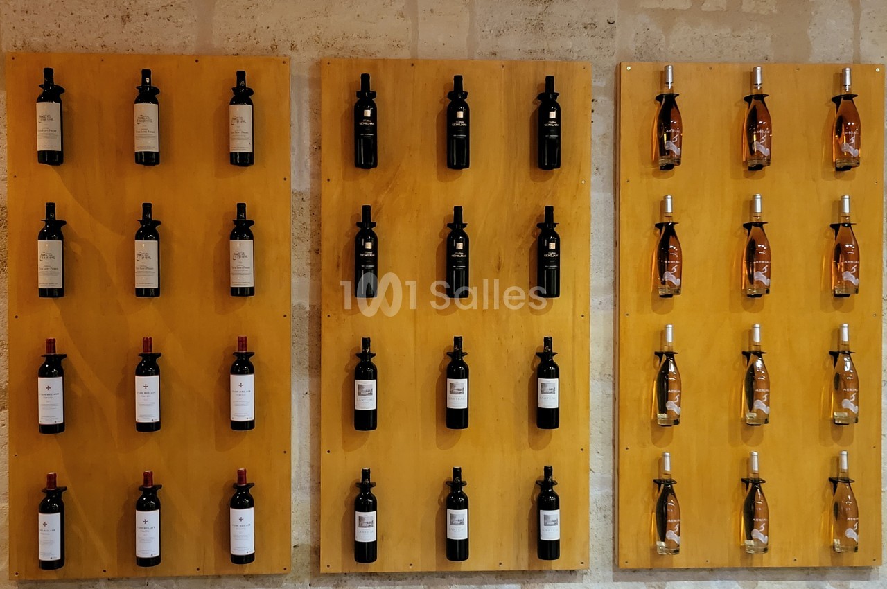 Bouteilles de vin alignées sur trois panneaux en bois fixés à un mur en pierre.