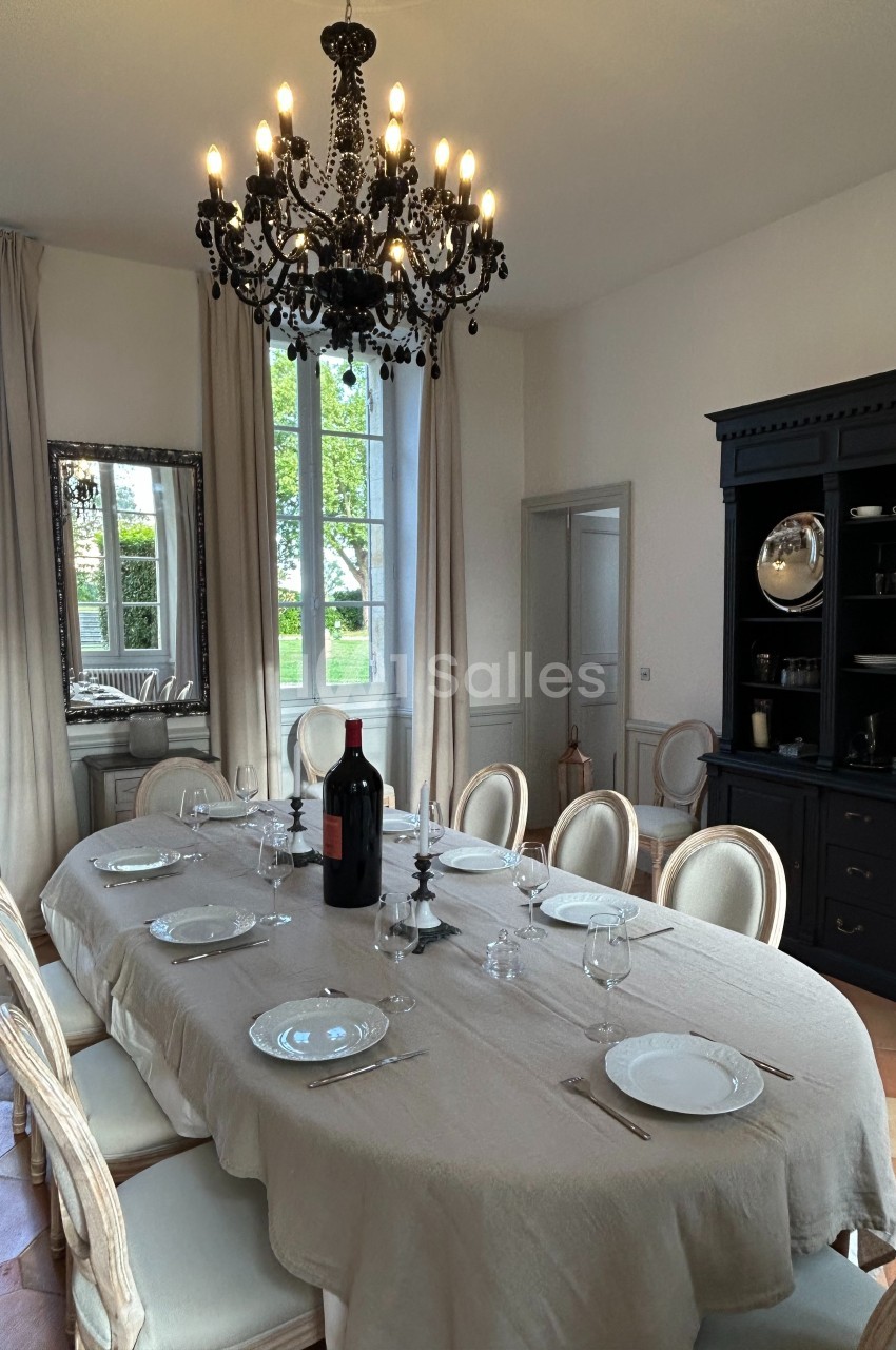 Salle à manger élégante avec une grande table dressée, un lustre noir, des chaises classiques et un buffet en arrière-plan.