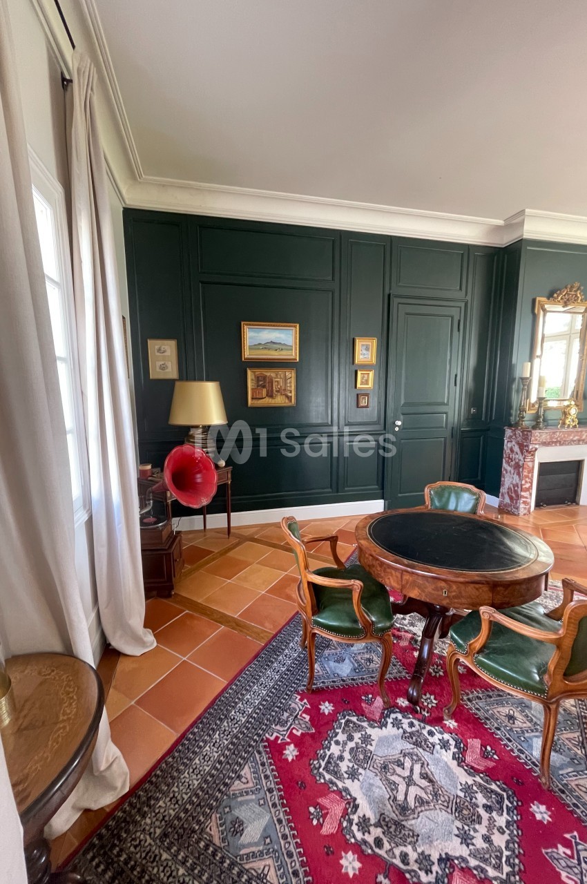 Salle de séjour élégante avec murs verts, table ronde en bois, gramophone rouge et cheminée ornée d'un miroir.
