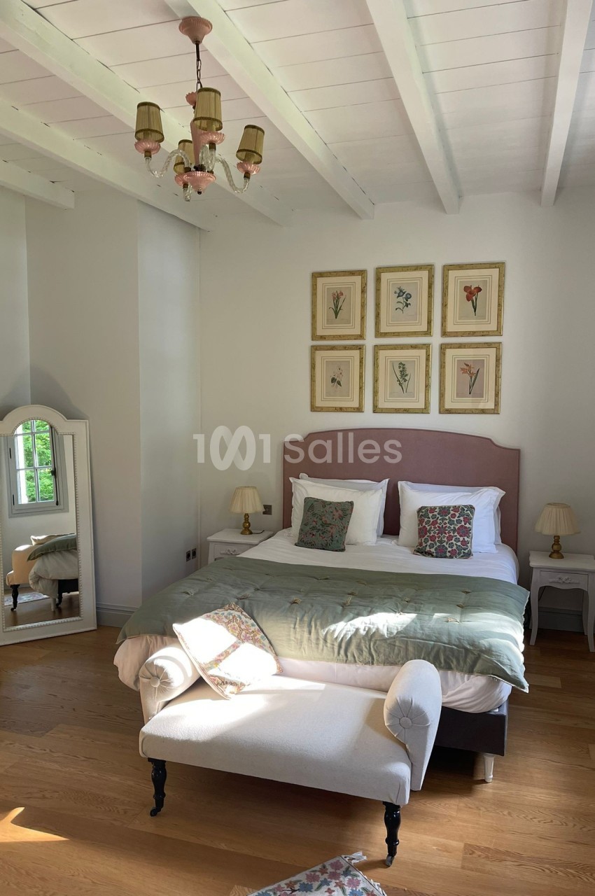 Chambre lumineuse avec lit double, coussins décoratifs, miroir sur pied, lustre et parquet en bois clair.